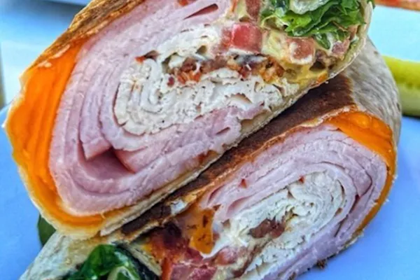 Enjoy a warm flour tortilla spread with creamy mayo and bold Dijon mustard, filled with antibiotic-free turkey, savory ham, crispy thick-cut bacon, fleshly sliced tomatoes, American cheddar cheese, and fresh organic spring mix for a delightful crunch.